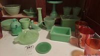 Assorted green glass items arranged on a shelf including juicers, small bowls, and containers.