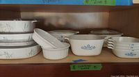 Multiple CorningWare bakeware pieces arranged on shelf featuring a variety of floral patterns and some lids.