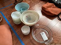 Overview of mixing bowls set on hardwood floor showing jadeite bowls, tulip pattern bowls, plain milk glass bowls and clear glass dish