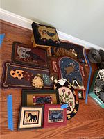 Overview of all hooked rugs, the stool, and framed hooked rug art pieces displayed together on floor.