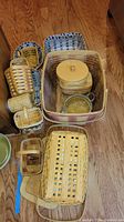 Overview of the collection of Longaberger baskets in various sizes and shapes with some liners and a lidded basket box, arranged on a wooden floor.