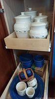 Photo of four cream-colored lidded canisters with blue floral and wave decorations in a wooden drawer.