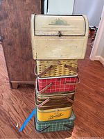 Stacked view of five tin bread baskets below a vintage metal roll-top bread box