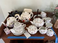 Photo showing assortment of tea pots including Noritake set with pink rose floral pattern, creamer, sugar bowl, six cups and snack saucers. Additional teapots with various designs, tea cozy and infuser included.