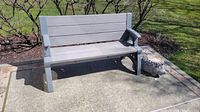 Full view of grey plastic bench on outdoor tiled surface with hedgehog decoration to the right side.