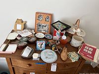 Overview of the lot showing plates, framed prints, tins, hand mirrors, and a basket with craft materials.