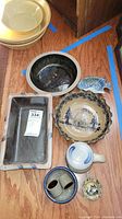 Photo showing most of the pottery pieces grouped on the floor including bowls, rectangular tray, fish-shaped plate, cabin plate, and mug with lid.