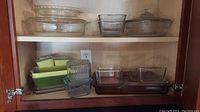 Shelf with assortment of clear glass rectangular and round dishes with lids, green and yellow glass dishes stacked horizontally.
