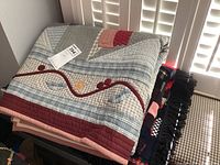 Folded view of stack of three quilts showing varied patterns and colors including patchwork and applique details