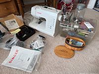Overview of Singer sewing machine with power cord, foot pedal, manual, and accompanying notions and tools arranged around it.