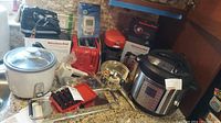 Overview of all kitchen appliances and tools on countertop showing boxed KitchenAid hand mixer, Instant Pot pressure cooker, KitchenAid food chopper, Bella coffee maker, Cuisinart toaster, mandolin, food mill, and grater.