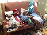 Wide shot showing multiple assorted throw blankets on a red checkered couch, some folded and some draped, including packaged sets.