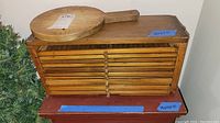 Front view of vintage wooden cigar drying box with multiple drawers and round wooden cutting board placed on top, showing surface details and dimensions tape.