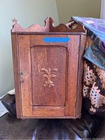 Front view of vintage wooden corner wall cabinet with a key lock and carved floral design on the door.