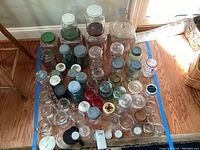Overview of 40+ heavy glass jars with assorted lids mostly green, blue, and some white and rusted metal scattered on floor.