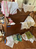 Wide view of vintage linens spread and draped over a wooden chest, including tablecloths, doilies, pot holders, and tea towels.