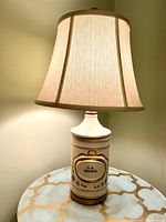 Full view of the porcelain apothecary jar lamp with beige fabric lampshade lit on a decorative table.