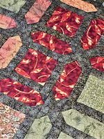 Close-up showing red, green, and beige fabric pieces with leaf and botanical patterns on a dark background with swirling design stitching.