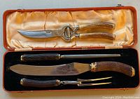 Full view of the carving set inside the orange lined box showing carving knife, fork, sharpening steel, and poultry shears with antler-style handles.