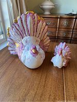 Front view of large and small pink and gold ceramic hens showing feather and floral designs