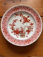 Top view of a single Royal Crown Derby porcelain plate showing red floral pattern with gold rim, placed on a wooden table.