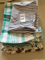 Five folded cotton dish towels with various patterns, including striped and checkered, stacked on each other with a label saying 'Lot 58' on top towel.
