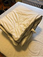 Folded white synthetic duvet with beige trim on a white textured mattress cover.
