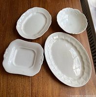 Four white ironstone platters and bowl arranged on wooden table showing shapes and embossed edges.