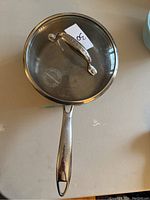 Top view of a Lagostina stainless steel saucepan with a tempered glass lid showing handle with Lagostina branding.