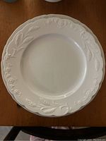 White ironstone dinner plate showing embossed botanical patterns on rim.