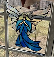 Large blue stained glass angel held by hand in front of a window, showing translucent textured glass wings and robe with a small crack