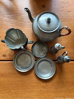 Top-down view of all items in set on wooden surface showing teapot with wood handle, sugar bowl, creamer, salt and pepper shakers, and three coasters