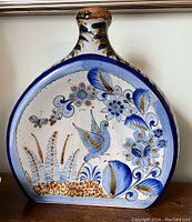 Front view of Mexican Tonola shoulder vase showing hand painted blue and brown birds and floral patterns.