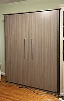 Closed grey wood-grain laminate Murphy bed cabinet with two vertical brushed metal handles