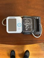 Digital blood pressure monitor with screen, control buttons, and attached arm cuff placed on wooden surface.