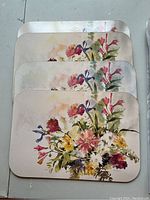 Four cork placemats stacked showing colorful floral designs with multiple flower types and green leaves on rounded rectangular placemats.