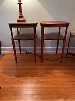 Two matching wooden side tables, one with glass top and one without, shown side by side on hardwood floor against a wall. Lamp on one table for size reference.