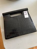 Front view of the rectangular black leather clutch showing glossy crocodile/alligator textured pattern and built-in handle cut-outs