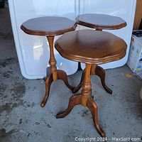 Set of three wooden Queen Anne style occasional tables shown standing on floor. Tables have scalloped oval tops with turned pedestal central column and three legs.