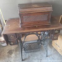 Antique Singer sewing machine table with wooden shelf top, brass hardware on drawers, and cast iron treadle base.