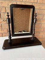 Full view of the antique vanity mirror showing dark stain wood frame, rectangular mirror, two turned wooden supports and base.