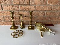 Photo of two brass candlesticks, a small pitcher, trivet, and corkscrew against brick background