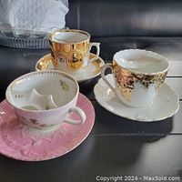 Three china teacups with built-in moustache guards and matching saucers in various colors and patterns.
