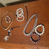 Photo showing the lot arranged on a wooden surface, items spread out and visible including gold-tone tubular necklace, various bracelets, rings, and necklaces.