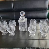Photo of crystal decanter with faceted stopper surrounded by eight brandy glasses.