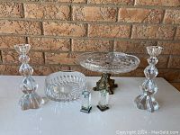 Full view of crystal serving lot on white table against brick wall background, showing candlesticks, cake tray, bowl, and salt and pepper shakers