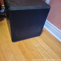 Front and side view of black Energy AS-90 subwoofer with cloth grille on wooden floor, showing good condition with minor surface wear.