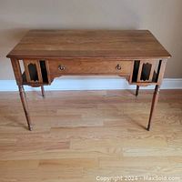 Front view of solid walnut desk showing center drawer with brass ring pull handles and open shelves on either side. Four turned tapered legs visible.