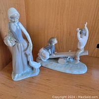 Frontal view of both porcelain figurines featuring the boy and girl on a seesaw and the woman with a goose.