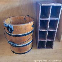 Metal banded wooden barrel with two side handles and natural wood finish placed beside rustic wooden divided crate with eight compartments.